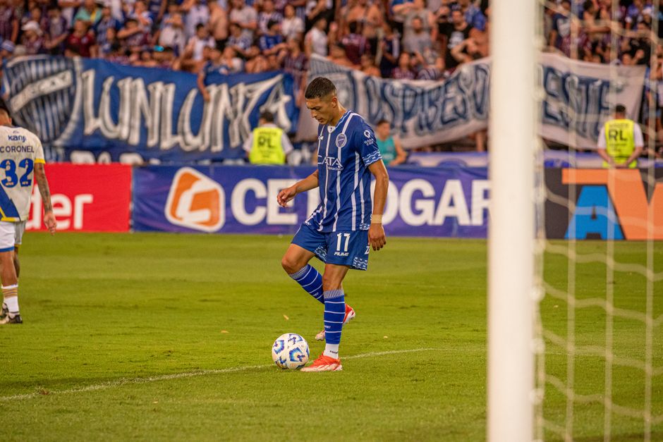 A soccer player in blue dribbles the ball during an outdoor football match.