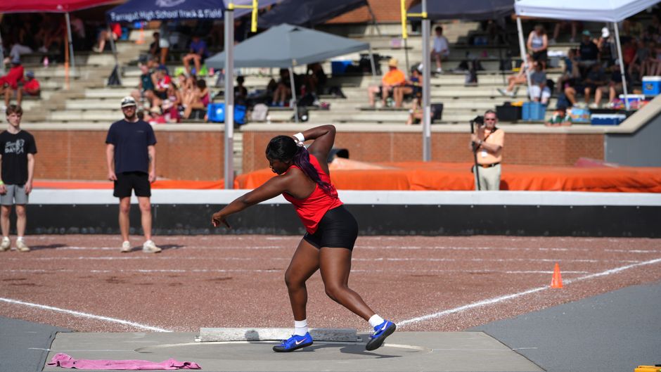 Female athlete performing shot put at an outdoor track and field competition.