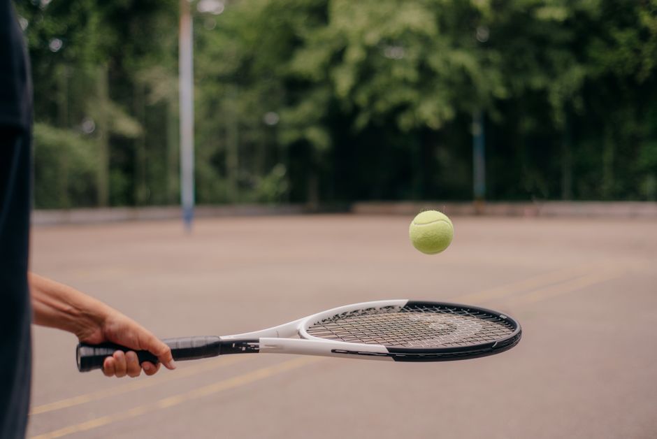 Close-up of a tennis racket and ball in an outdoor court setting.