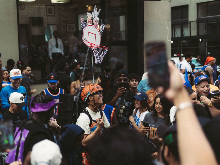 Vibrant street scene of basketball fans wearing jerseys and celebrating with a mini hoop setup.