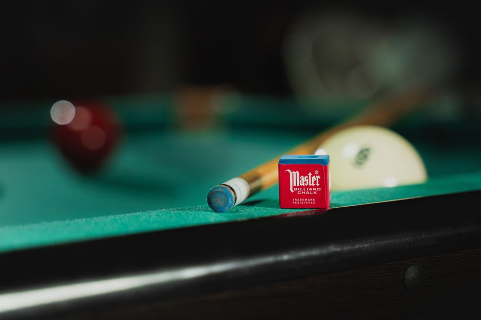 Close-up of billiard chalk, cue stick, and ball on a pool table.