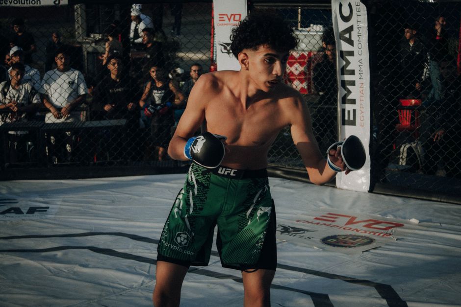 Young male fighter in action during an MMA fight in a cage.
