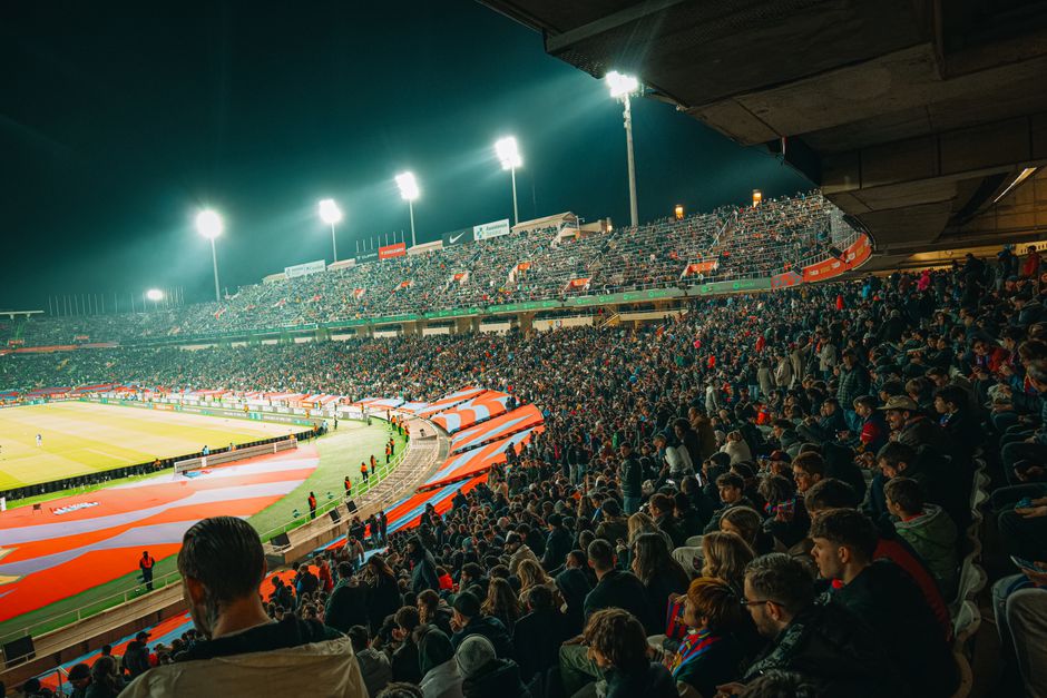 A vibrant nighttime soccer match with a packed stadium full of enthusiastic fans.